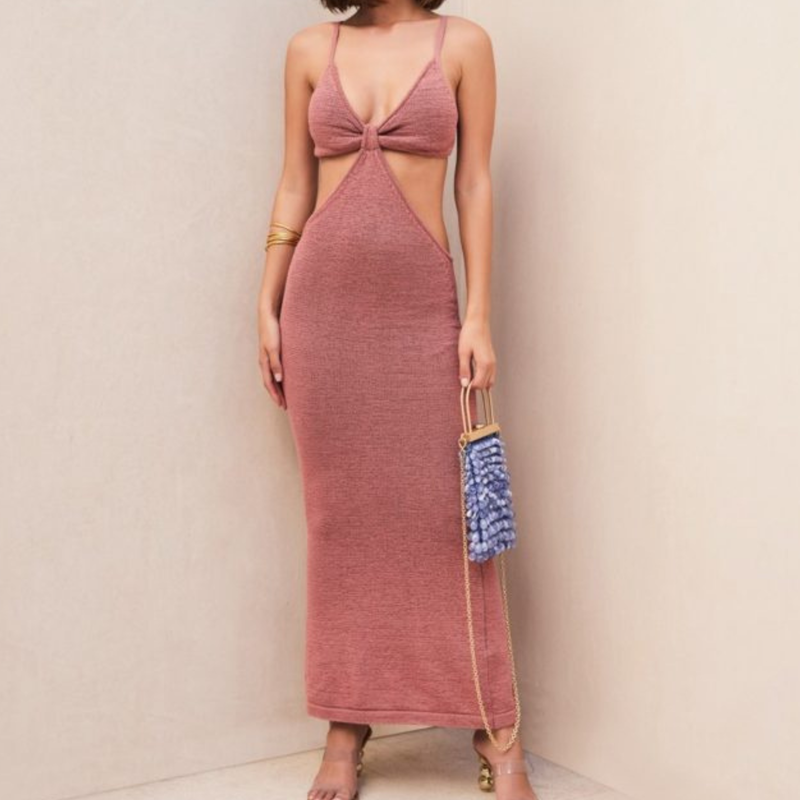 Woman wearing a pink dress with a slit, holding a blue clutch against a beige background